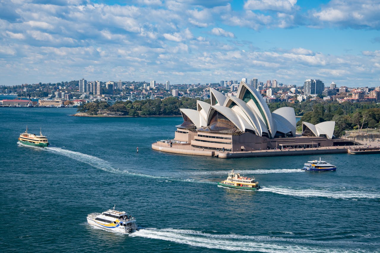 Home Stunning aerial photograph capturing Sydney Opera House and busy harbor ferries on a sunny day.