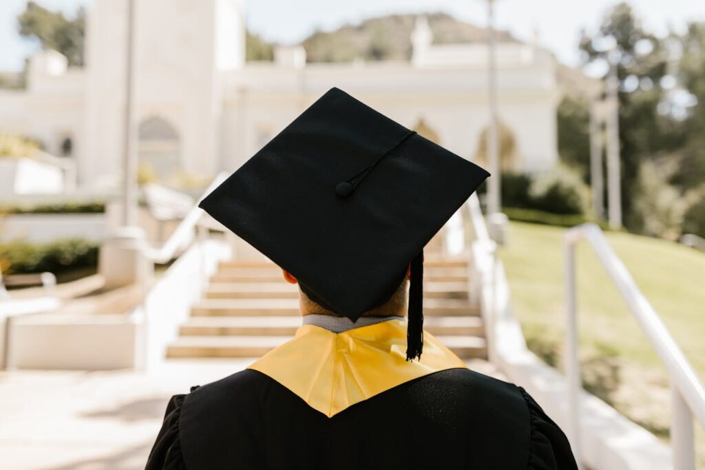 Hello world! Back view of a graduate in a cap and gown standing outdoors facing a building.