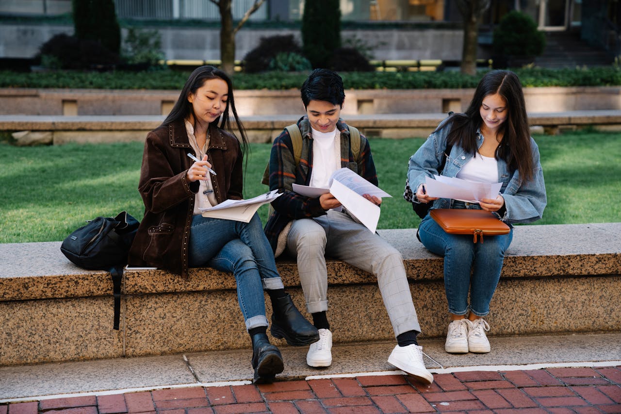 services-01 Three students studying together on a bench in a university campus setting outdoors.